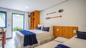 A hotel room with two beds, a wooden headboard, a small table with a kettle, and a view of greenery outside.