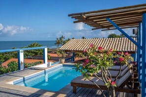 A pool area with a view of the ocean, wooden deck, and lounge chairs. - Vila Maria Pousada (Jijoca de Jericoacoara)