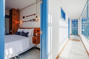 Habitación de hotel con cama, cabecero de madera, luces empotradas en la pared y una puerta azul.