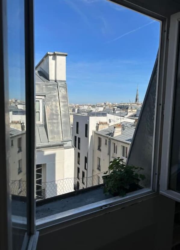 Vista da janela sobre uma paisagem urbana com vários edifícios, incluindo um prédio branco de destaque com telhado inclinado.