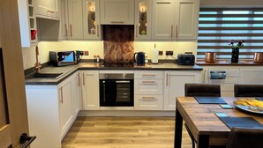 A modern kitchen with white cabinetry, a built-in oven, a coffee machine, and a dining area with a wooden table and chairs.
