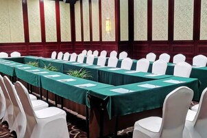 Un salón de conferencias con filas de mesas y sillas, manteles verdes y fundas blancas para las sillas.