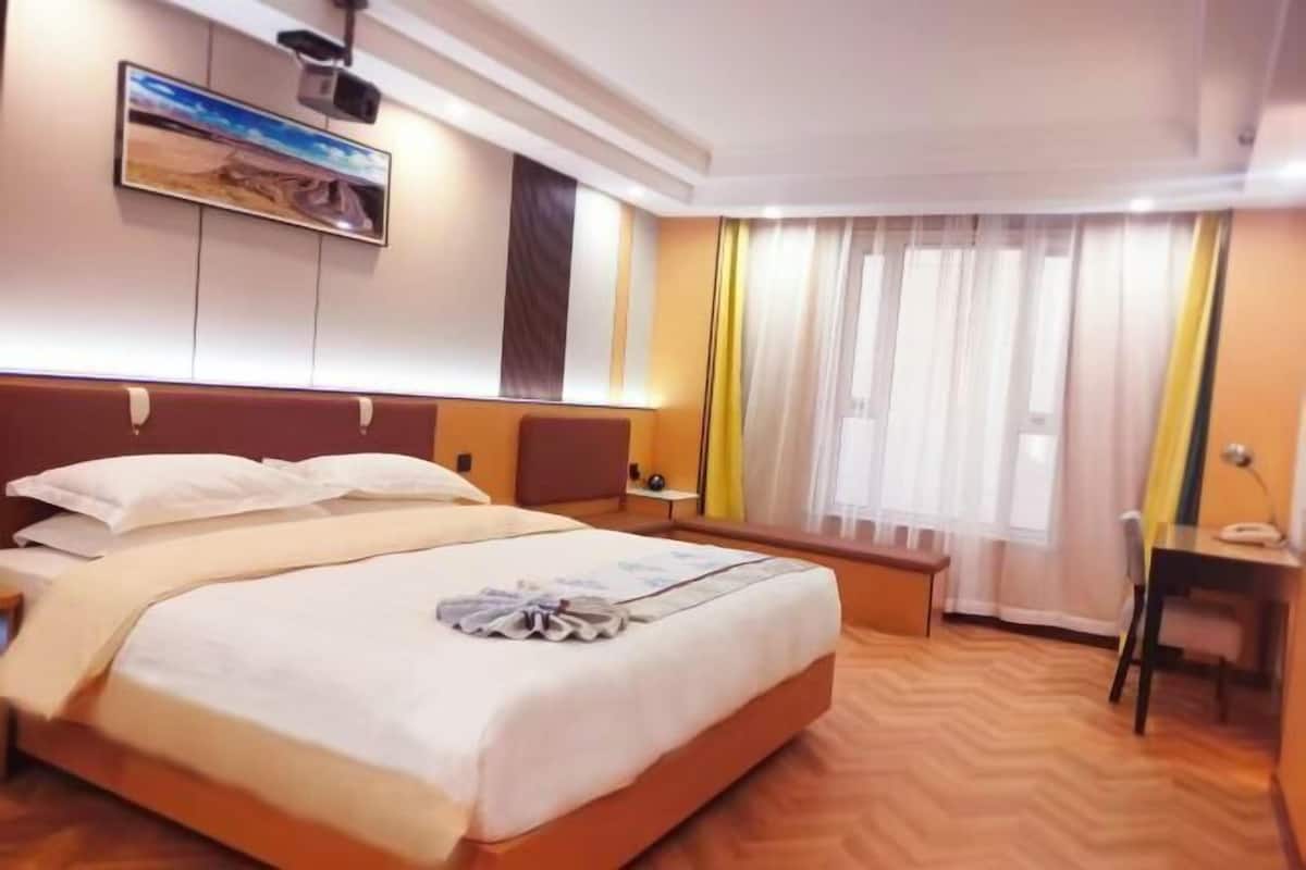 A hotel room with a bed, a desk, a chair, a window with curtains, and a wall-mounted TV.