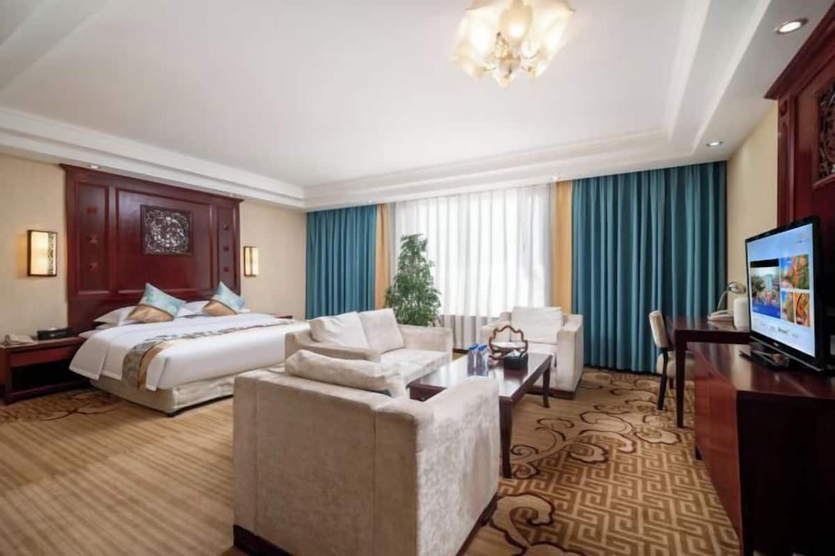 A hotel room with a bed, two armchairs, a sofa, a TV, and a desk.