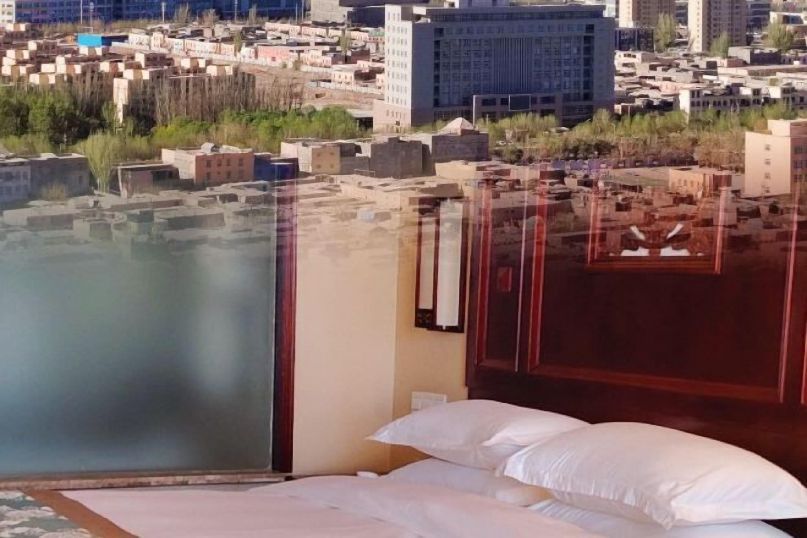 A hotel room with a bed, a view of a cityscape, and a window with a reflection.