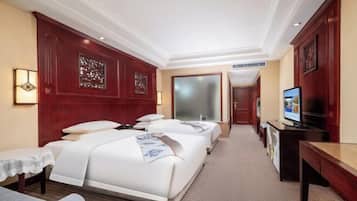 A hotel room with two beds, a desk, a TV, and a small table with a lamp.