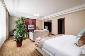 A hotel room with a bed, a desk, a chair, a television, and a potted plant. - Kashi Laining Hotel (Kashgar City)