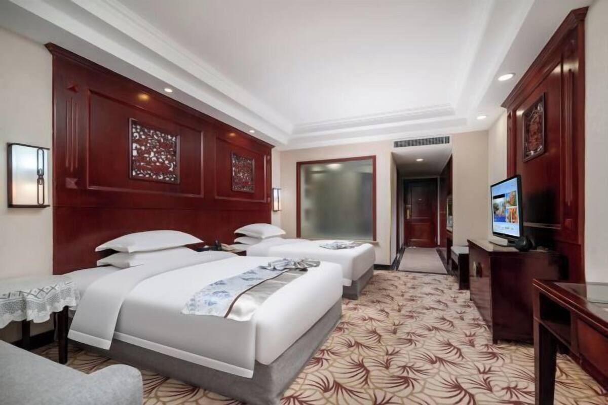 A hotel room with two beds, a TV, a desk, and a patterned carpet.