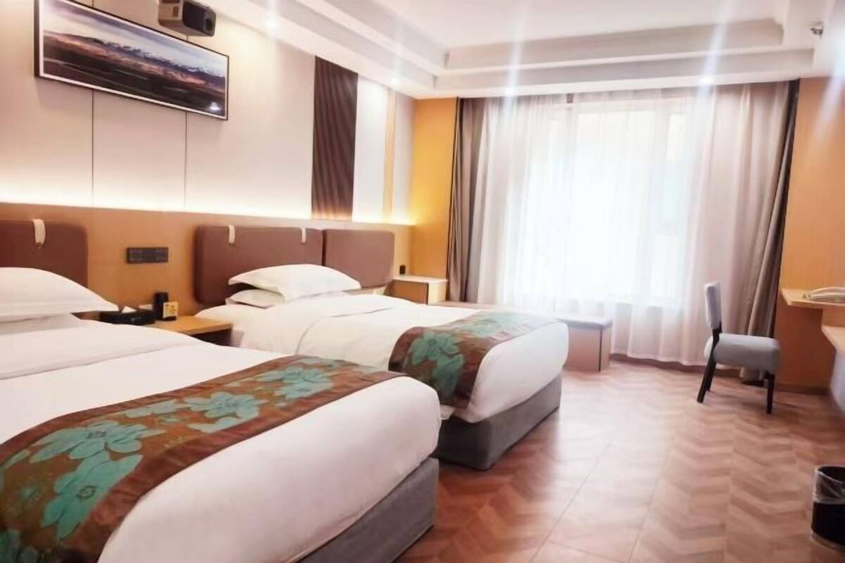 A hotel room with two beds, a desk, a chair, and a large window with curtains.