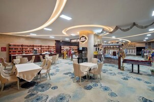 Interior de restaurante con mesas, sillas, una alfombra estampada y estanterías con objetos.