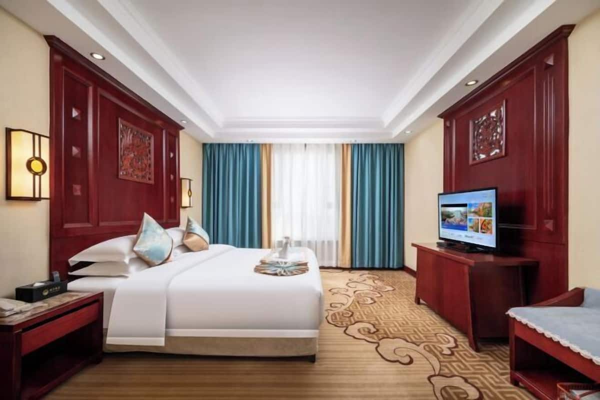 A hotel room with a bed, a television, a desk, and a window with curtains.