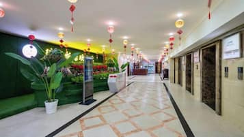 Un pasillo de hotel con suelo de baldosas, plantas en macetas y faroles rojos.