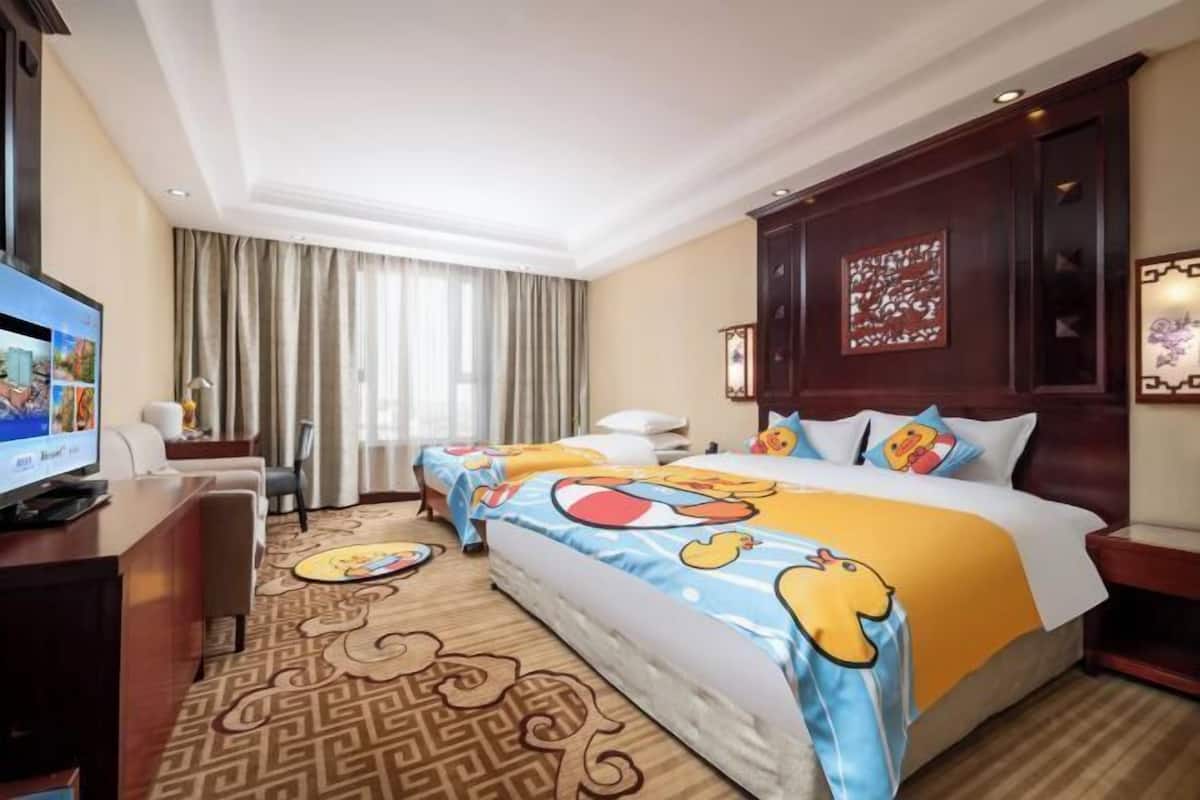A hotel room with two beds, a television, a desk, and a patterned carpet.