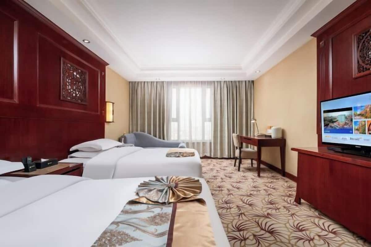 A hotel room with two beds, a television, a desk, and a chair.