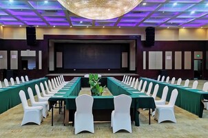 Un salón de conferencias con mesas largas y sillas blancas, una pantalla grande y un escenario.