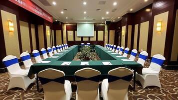 Un salón de conferencias con una larga mesa, sillas con cintas azules y una pantalla de proyector.