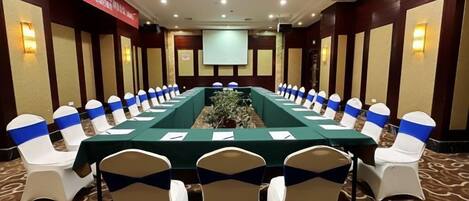A conference room with a long table, chairs with blue sashes, and a projector screen.