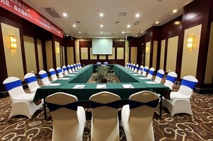 Un salón de conferencias con una larga mesa, sillas con cintas azules y una pantalla de proyector.