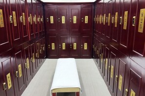 A row of dark wooden lockers with gold handles and numbers, a white bench in the center, and a carpeted floor. - Kashi Laining Hotel (Kashgar City)