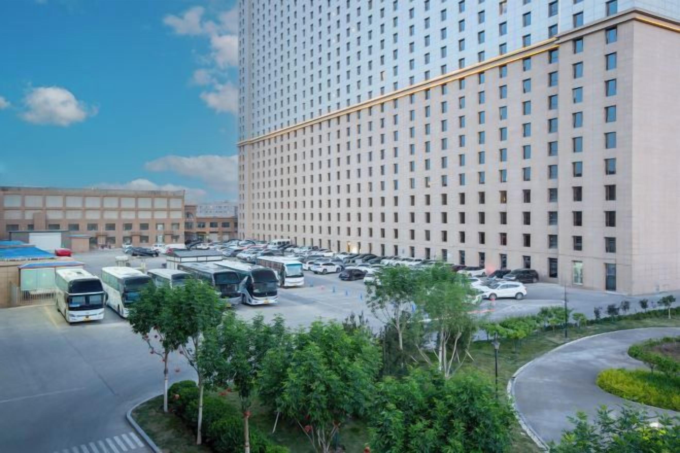 A large hotel with a parking lot and a landscaped area with trees.