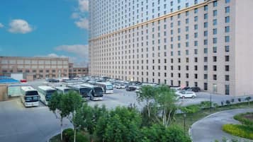 A large hotel with a parking lot and a landscaped area with trees.