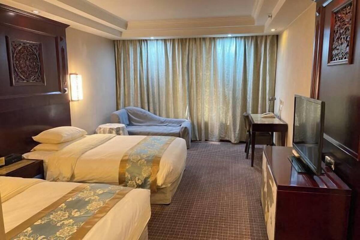 A hotel room with two beds, a desk, a chair, a television, and a window with curtains.