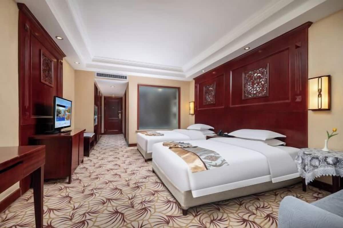 A hotel room with two beds, a TV, a desk, and a patterned carpet.