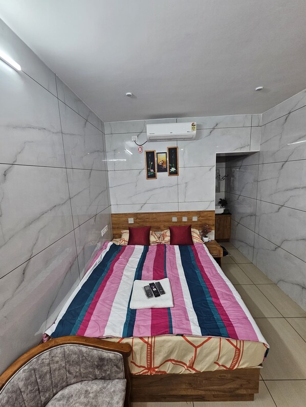 Un dormitorio con cama, una silla, una mesita de noche, un equipo de aire acondicionado y un armario pequeño.