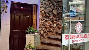 Entrada de hotel con un muro de piedra, una escalera y un letrero que indica 'Rooms Available'.