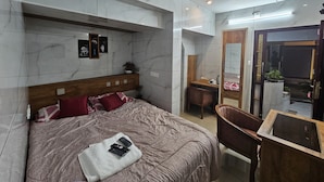 Un dormitorio moderno con pared de mármol, cabecero de madera, cama con ropa de cama roja y blanca, una mesita de noche, una silla y un pequeño escritorio con un espejo.