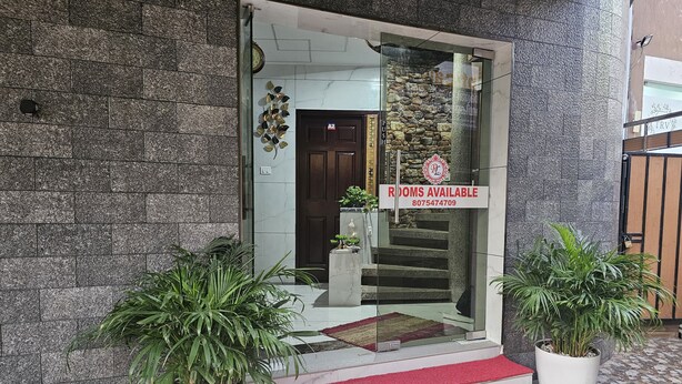 Entrada de hotel con un letrero que dice 'Rooms Available', una escalera y plantas en macetas.