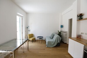 A modern kitchen with a glass table, a yellow chair, a covered sofa, and a radiator.