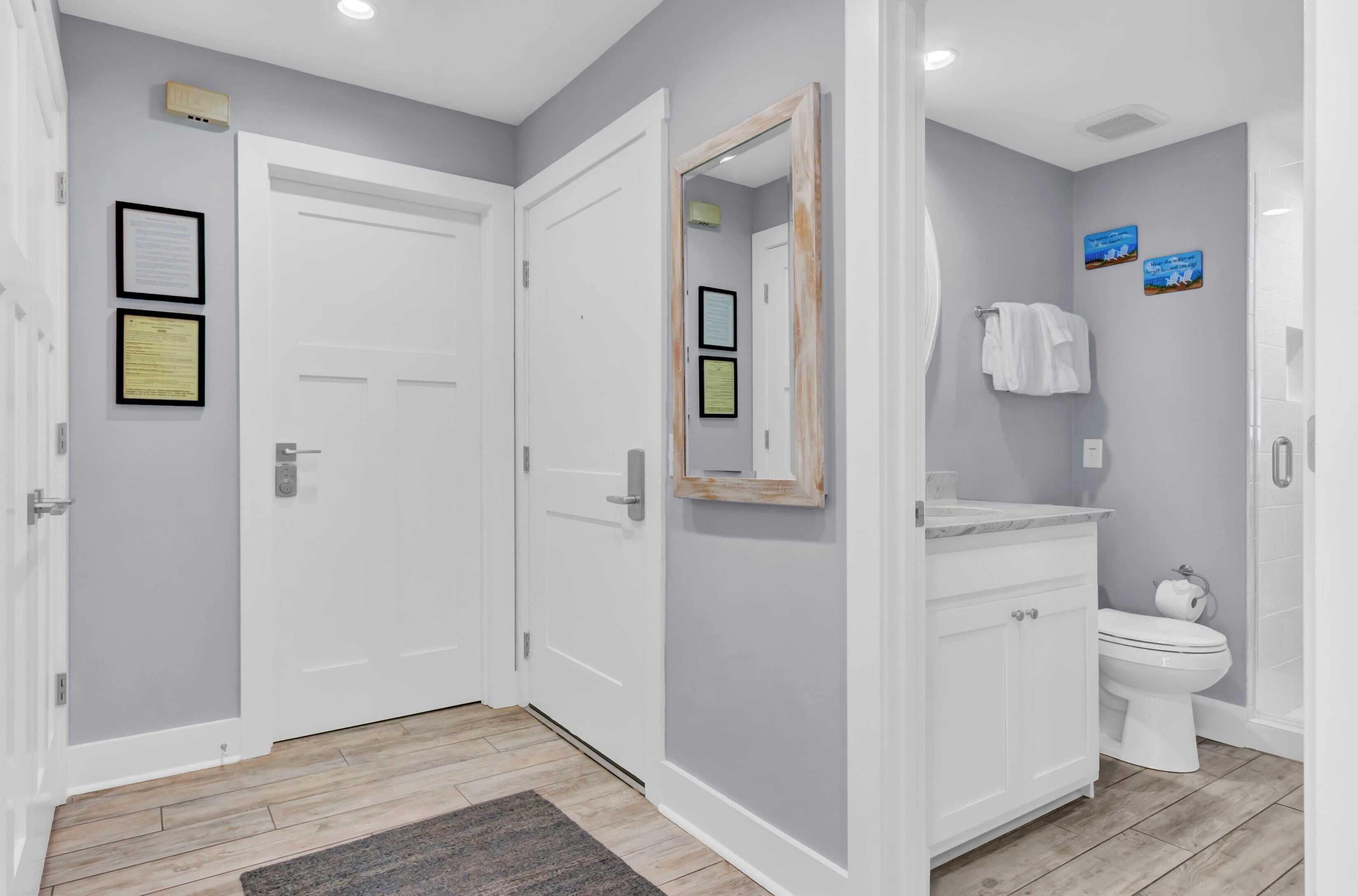 Une salle de bain avec des toilettes, un lavabo et un miroir. Des certificats encadrés sont accrochés au mur, et il y a un porte-serviettes avec des serviettes.