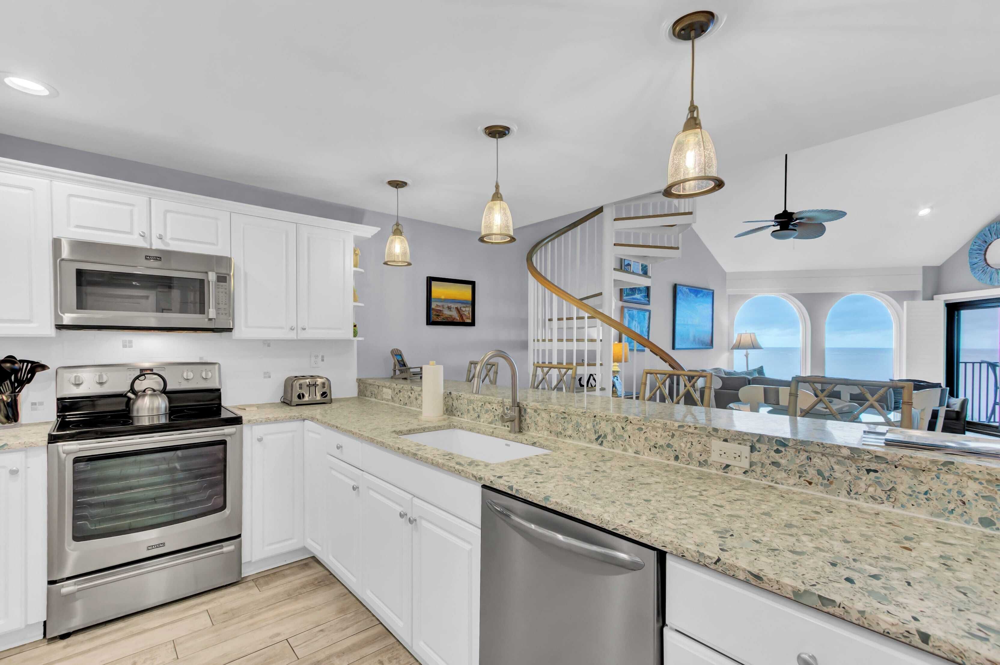 A modern kitchen with white cabinets, stainless steel appliances, granite countertops, and pendant lighting.