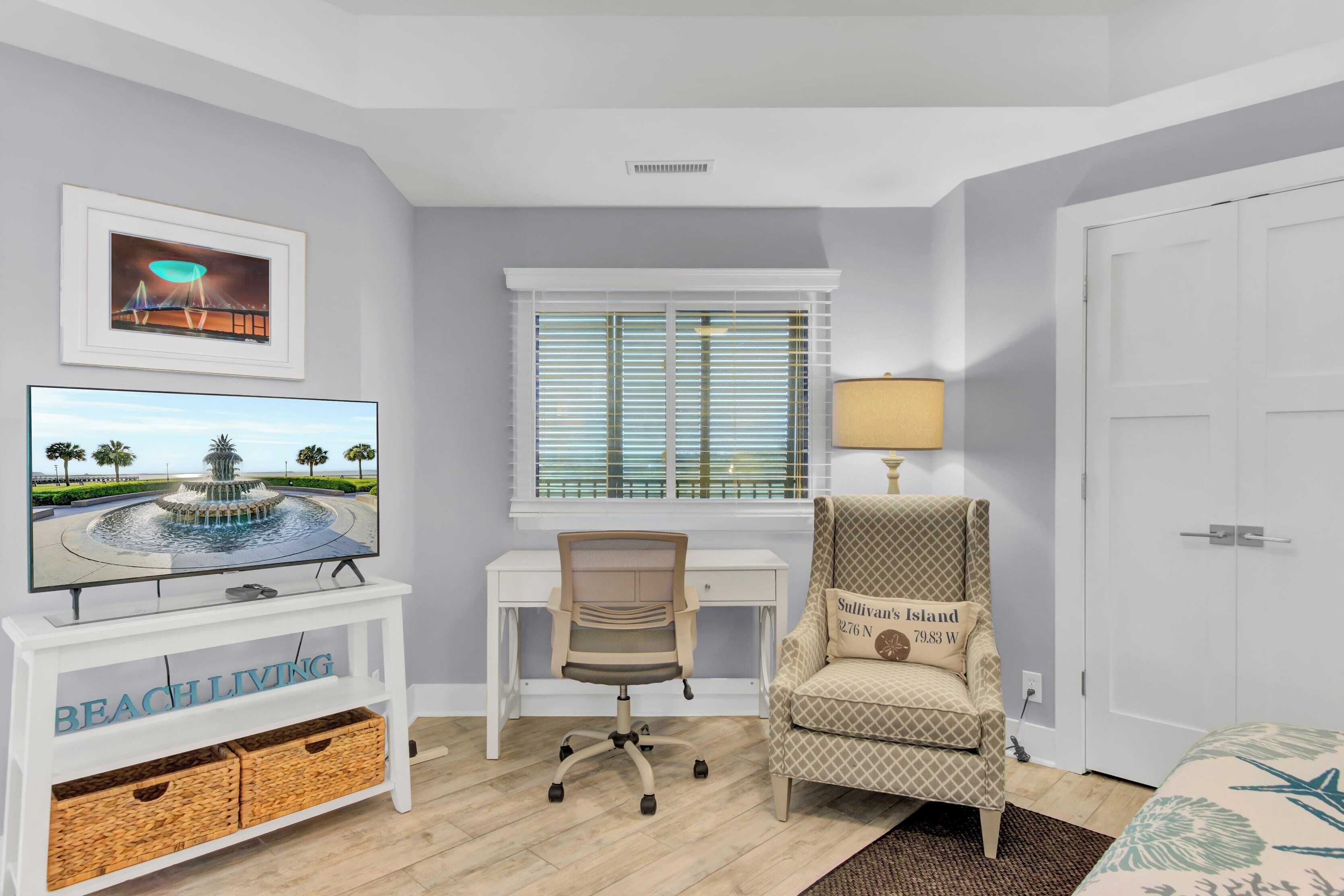A room with a white desk, a chair, a television, a lamp, and a bed.