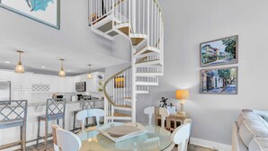 A modern kitchen with white cabinets, a glass dining table, and a spiral staircase. - 518 Seascape Waterfront Views + Community Pool (Isle of Palms)