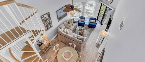 A spacious living area with a wooden staircase, a round dining table, and a large window offering a view of the outdoors.