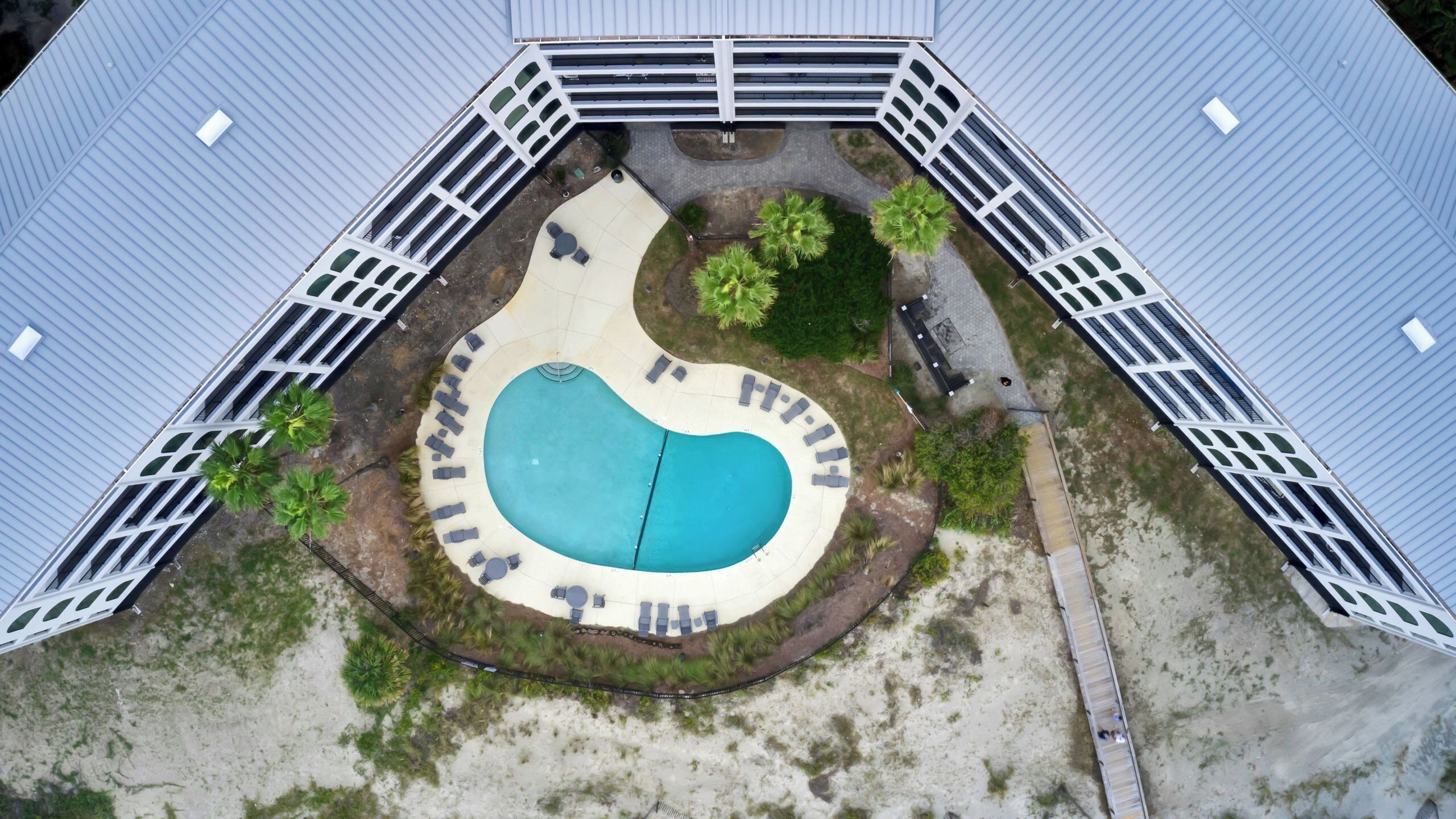 Vista aérea de una propiedad con piscina, terraza cubierta y jardín cercado.