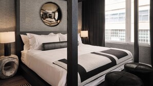 A modern hotel room with a large bed, a round mirror on the wall, and a view of the city through the window.