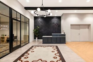 Un espace de bureau moderne comprenant un comptoir d’accueil, une grande plante en pot et un tapis à motifs.