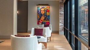 A modern interior with a long corridor, white armchairs, a colorful mural, and large windows.