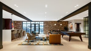 A modern lounge area with a pool table, comfortable seating, and a view of the city through large windows.