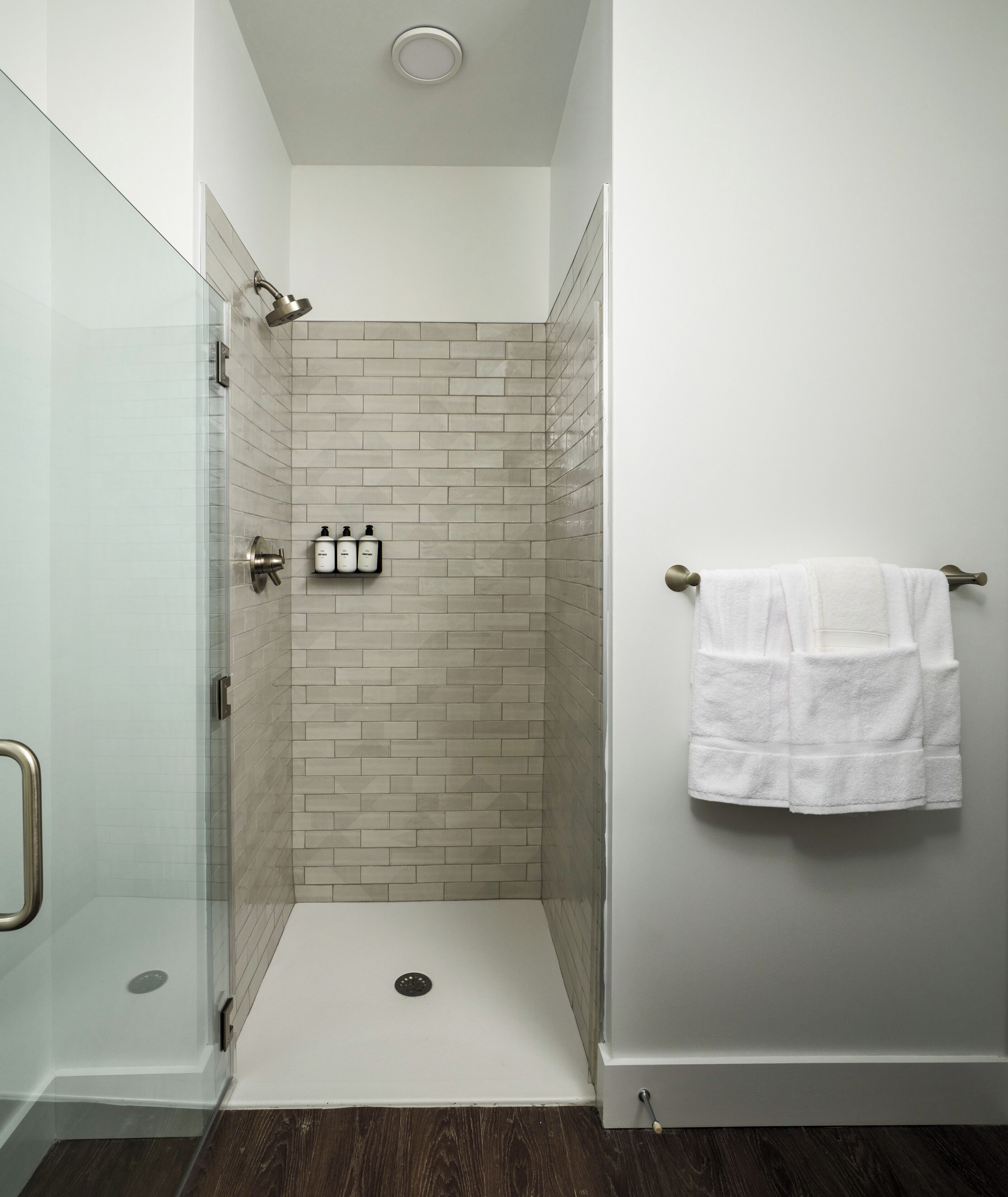 A modern shower room with a glass door, beige tiled walls, and a white towel hanging on the wall.