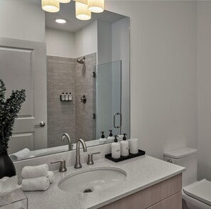 Une salle de bain moderne avec un grand miroir, un lavabo à deux robinets et un espace douche.
