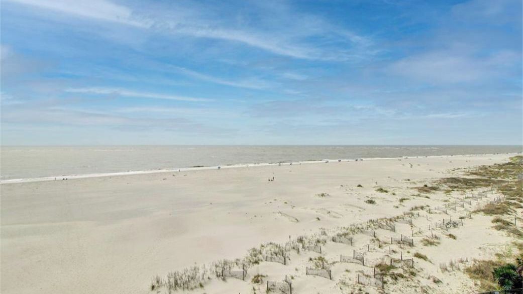 Une plage bordée d’une clôture, avec des dunes de sable et un ciel dégagé.