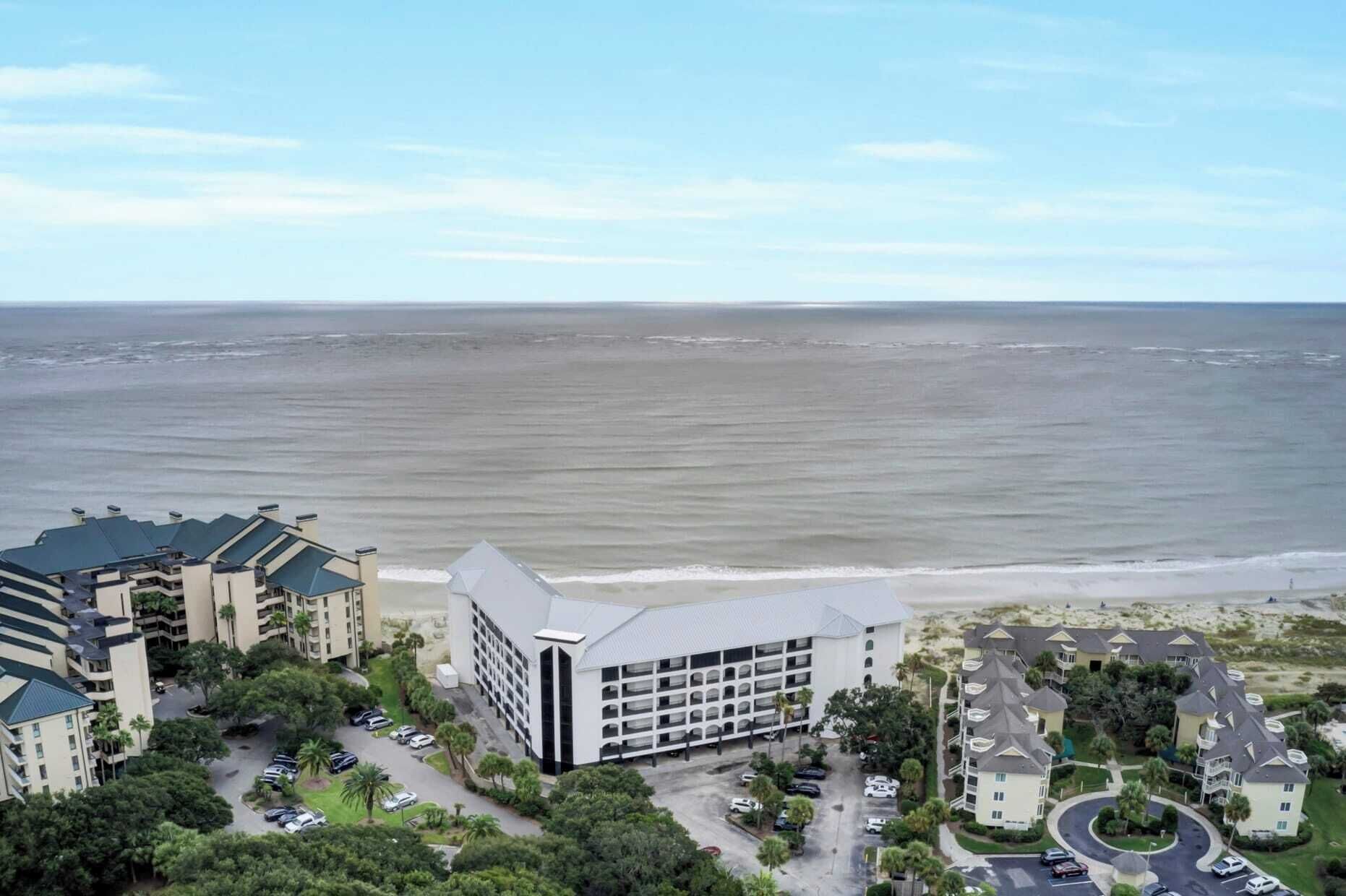 Un hotel costero con varias construcciones, un estacionamiento y vista al océano.