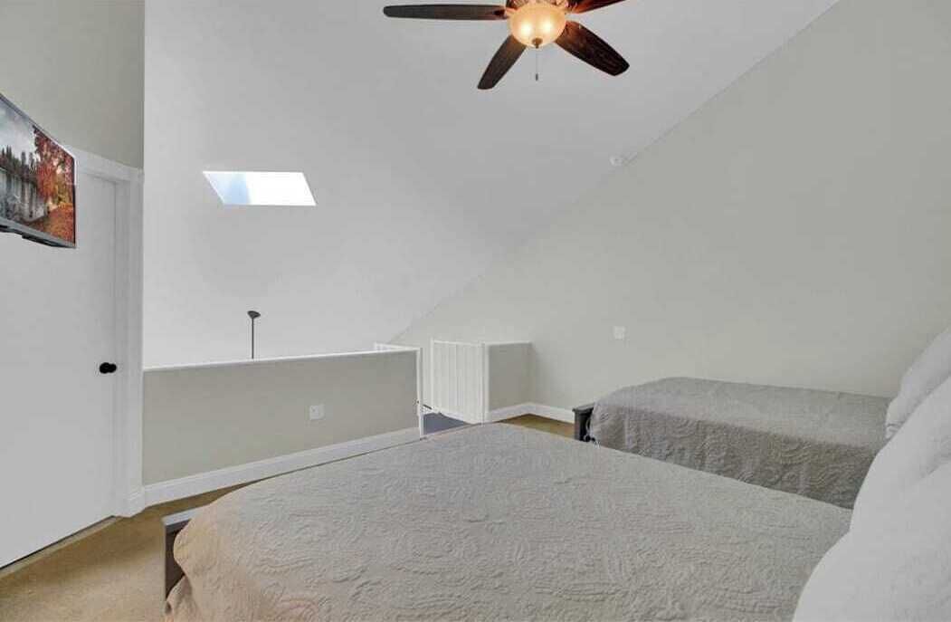 A bedroom with a sloped ceiling, a ceiling fan, a skylight, and a radiator.