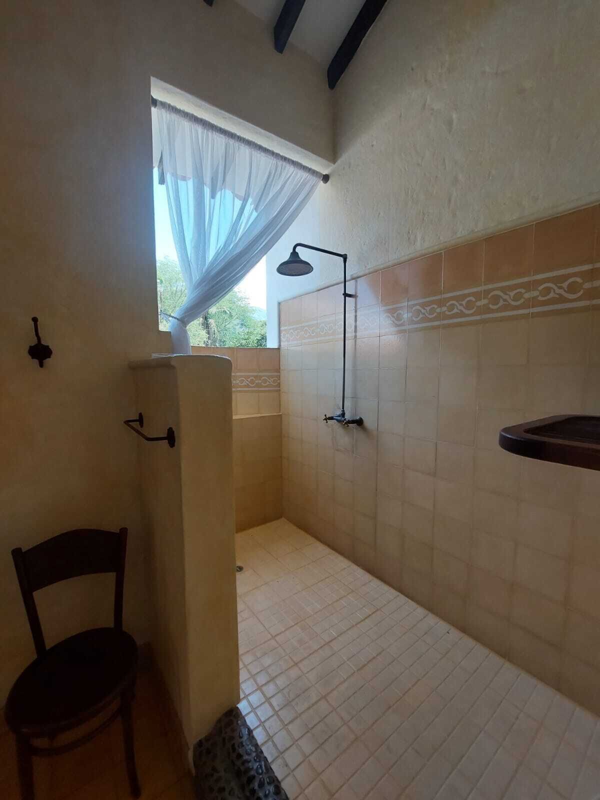 A bathroom with a shower, a chair, a window with sheer curtains, and a towel rack.