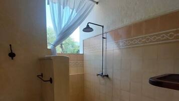 A bathroom with a shower, a chair, a window with sheer curtains, and a towel rack.