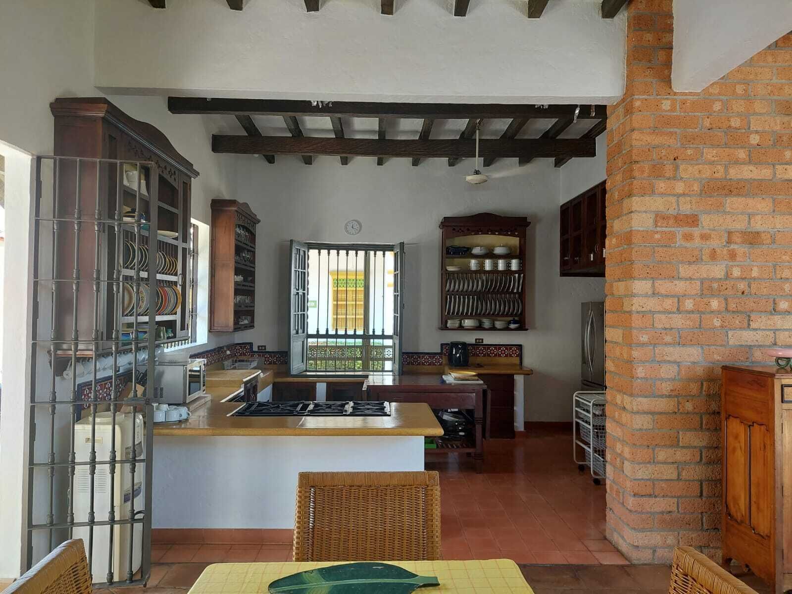 Una cocina con una isla central, un comedor con una silla de mimbre y una pared de ladrillo.